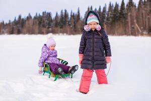 Adorable happy girl sledding her little sister photo