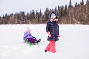 Adorable happy girl sledding her little sister photo