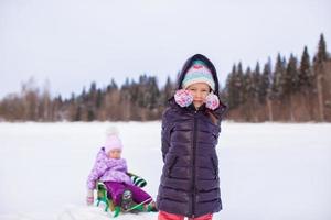 Adorable little happy girl sledding her sister photo