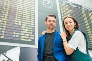 pareja joven en el aeropuerto internacional mirando el tablero de información de vuelo foto