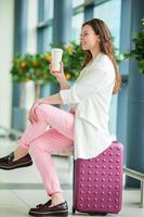 Young woman in international airport with her luggage and coffee to go waiting for her flight photo