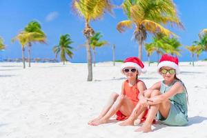 adorables niños pequeños con sombrero de santa durante las vacaciones navideñas en la playa. año nuevo en la playa foto
