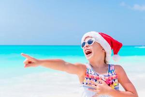 Adorable little girl in Santa hat during Christmas beach vacation photo