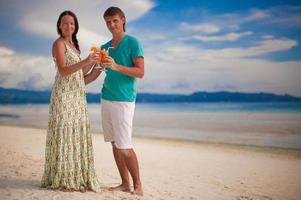 Young romantic couple relaxing with two cocktails on sandy beach photo