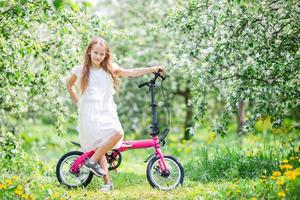 Adorable girl riding a bike at beautiful summer day outdoors photo