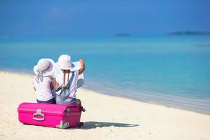 Little girls with big suitcase and map at tropical beach photo