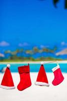 sombreros rojos de santa y calcetín de navidad colgando en la playa tropical foto