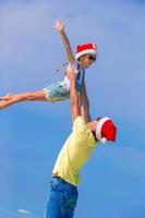 Little girl and happy dad in Santa Hat during beach vacation photo