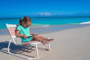 Little girl with laptop on beach during summer vacation
