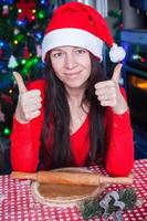 Young woman in Christmas hat raised thumbs up at home photo