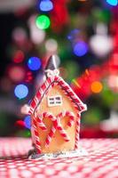 casa de pan de jengibre decorada con caramelos coloridos sobre un fondo de árbol de navidad brillante con guirnalda foto