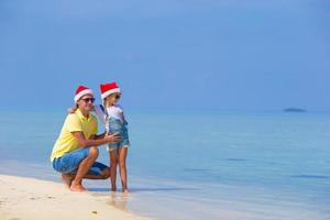 niña y papá feliz con sombrero de santa durante las vacaciones en la playa foto