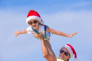 Little girl and happy dad in Santa Hat during beach vacation photo