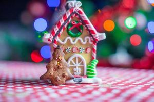 Gingerbread house decorated by sweet candies on a background of bright Christmas tree with garland
