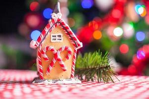 casa de hadas de pan de jengibre de primer plano decorada con dulces coloridos sobre un fondo de árbol de navidad brillante con guirnalda foto