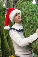 joven con sombrero de santa comprando un árbol de navidad foto