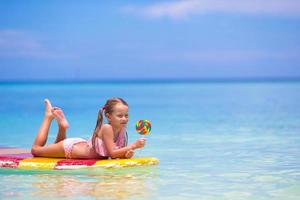 Little girl with lollipop have fun on surfboard in the sea photo