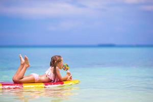 Little girl with lollipop have fun on surfboard in the sea photo