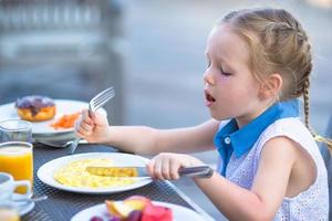 Adorable little girl having breakfast at outdoor cafe photo