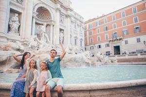 familia feliz tirando monedas en la fuente de trevi, roma, para la buena suerte. niñas y padres pidiendo el deseo de volver foto