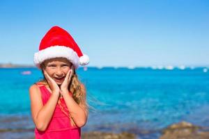Suprised little girl in christmas hat during beach vacation photo