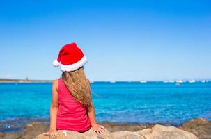 linda niña con sombrero de santa en la playa durante las vacaciones foto