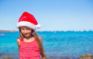 Cute little girl in Santa hat on the beach during vacation photo