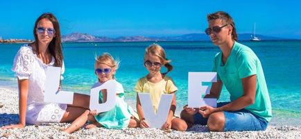 joven y hermosa familia de cuatro con palabra amor en la playa foto