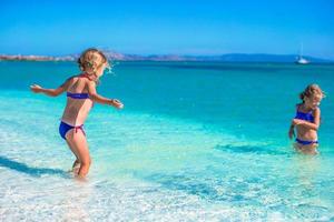 Adorable little girls have fun in shallow water at tropical beach photo