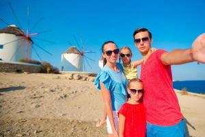 Family of four taking selfie with a stick in front of windmills at popular tourist area on Mykonos island, Greece photo
