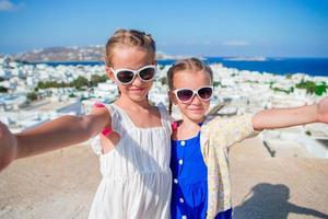 Two girls taking selfie photo outdoors with amazing view on greek village and sea