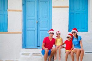 familia con sombreros de santa en vacaciones de navidad. padres e hijos en la calle del típico pueblo griego en la isla de mykonos, en grecia foto