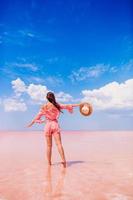 mujer con sombrero camina sobre un lago salado rosa en un día soleado de verano.