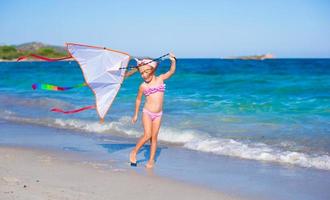 Little adorable girl playing with flying kite during tropical beach vacation photo