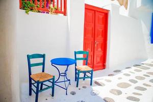 sillas azules y mesa en la calle del típico pueblo tradicional griego con casas blancas en la isla de mykonos, grecia, europa foto