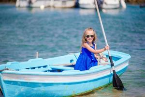 linda chica en bote azul en la bahía del mar cerca de la ciudad de mykonos en grecia. el niño pequeño disfruta nadando en el bote pequeño. foto