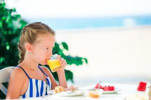 Adorable little girl having breakfast at cafe with sea view photo