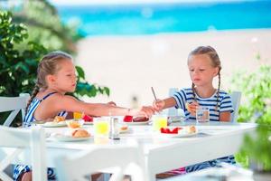 Lunch time. Little girls having breakfast at outdoor cafe with sea view photo