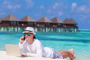 Young man with tablet computer and cell phone on tropical beach photo