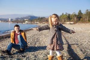 Adorable little girl with father having fun on beach in winter warm day photo