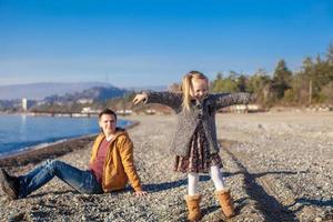 Adorable little girl with father having fun on beach in winter warm day photo