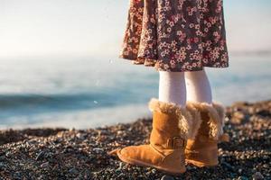 Closeup of legs little girl in cozy fur boots background the sea photo