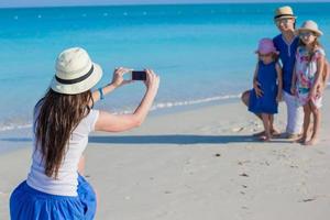 joven madre haciendo fotos en el teléfono de su familia en la playa