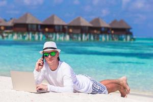 Young man with tablet computer and cell phone on tropical beach photo