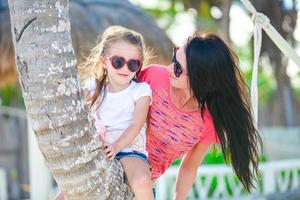 Happy mom and kid enjoying time together at the white beach on palm tree photo