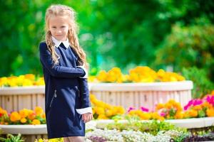 linda niña sonriente posando frente a su escuela el primero de septiembre. adorable niño pequeño que se siente muy emocionado por volver a la escuela foto