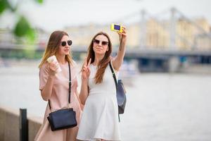 Caucasian girls making selfie background big bridge. Young tourist friends traveling on holidays outdoors smiling happy. photo