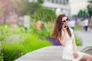 chica feliz habla por teléfono inteligente al aire libre en el parque. joven mujer atractiva con teléfono móvil al aire libre disfrutando de vacaciones destino de viaje en turismo y explorando el concepto foto