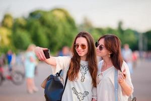 Caucasian girls making selfie outdoors. Young tourist friends traveling on holidays smiling happy. photo