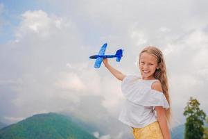 Happy little girl with toy airplane in hands in mountains photo